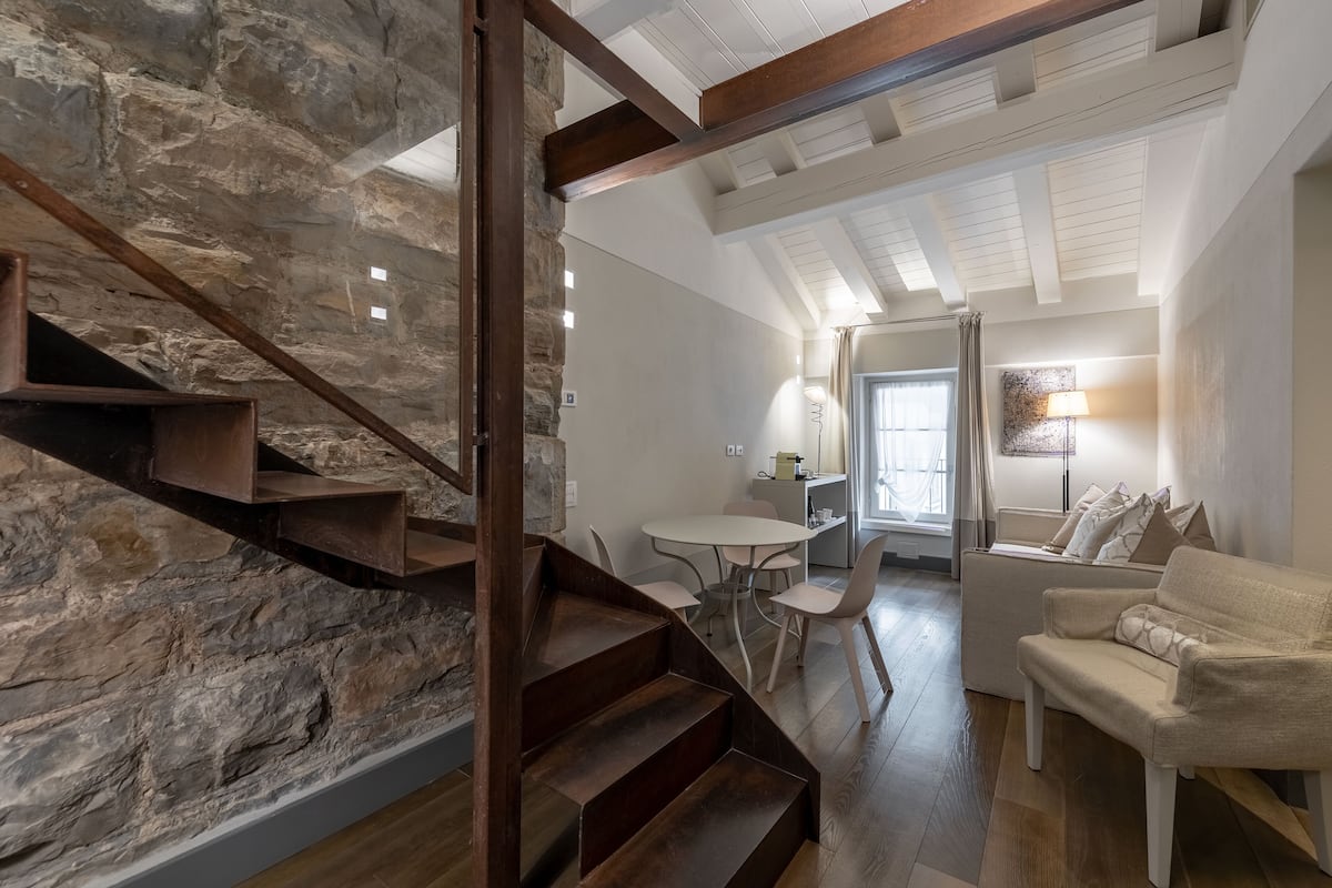 Un interior moderno con pared de piedra, escalera de madera y una zona de estar acogedora con sofá y sillones.