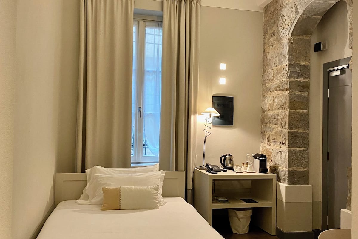 Una habitación de hotel con cama, escritorio con lámpara, cafetera y pared de piedra.