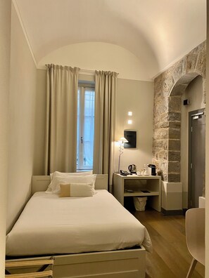 Een hotelkamer met een bed, een bureau met een lamp, een koffiezetapparaat en een stenen muur.