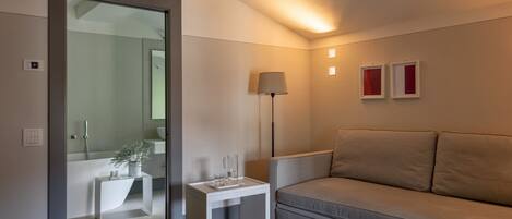 En moderne stue med sofa, sofabord, gulvlampe og en glasdør til et badeværelse.