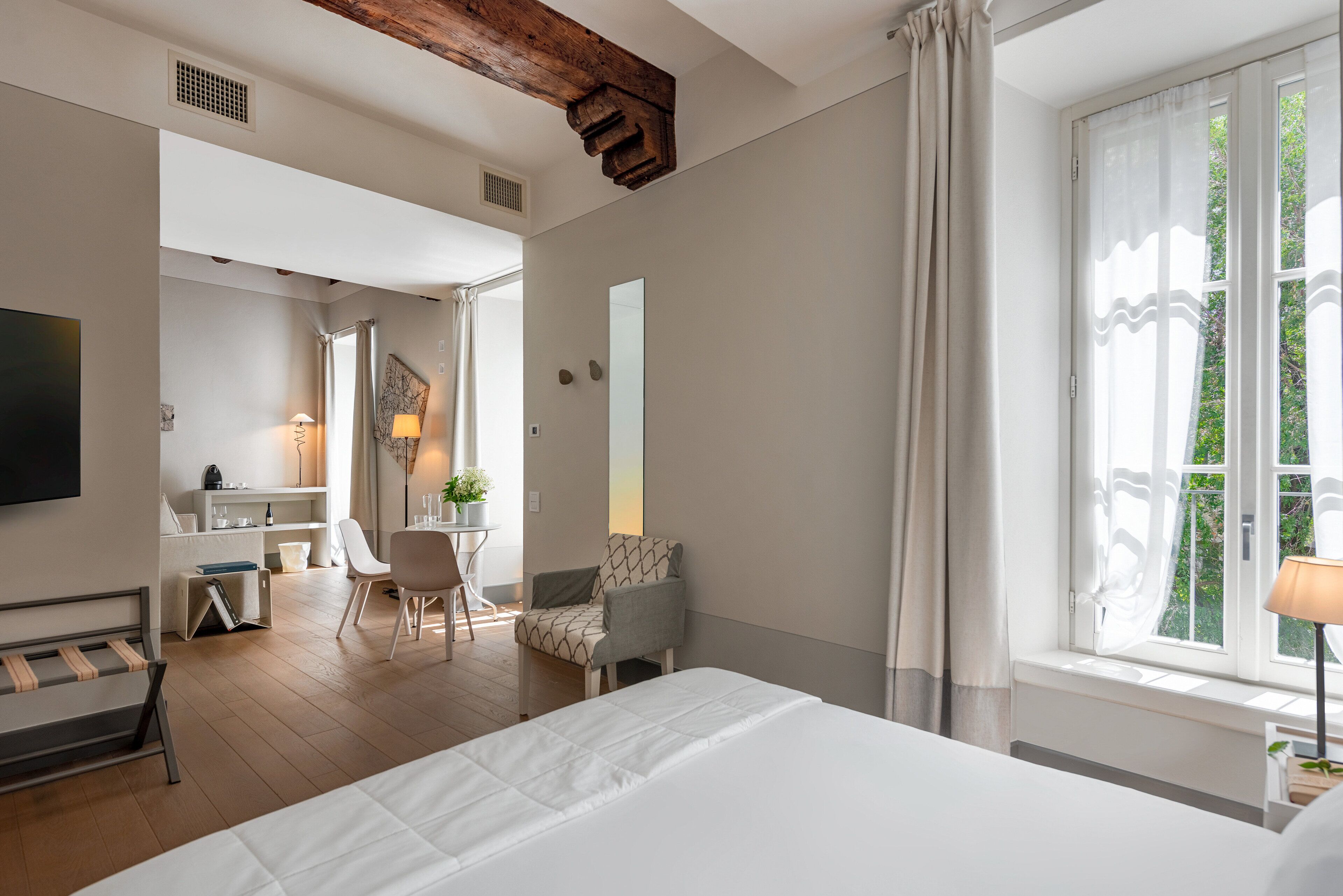 Una habitación de hotel moderna con una cama grande, un escritorio con una silla, una mesita con una lámpara y una ventana con cortinas.