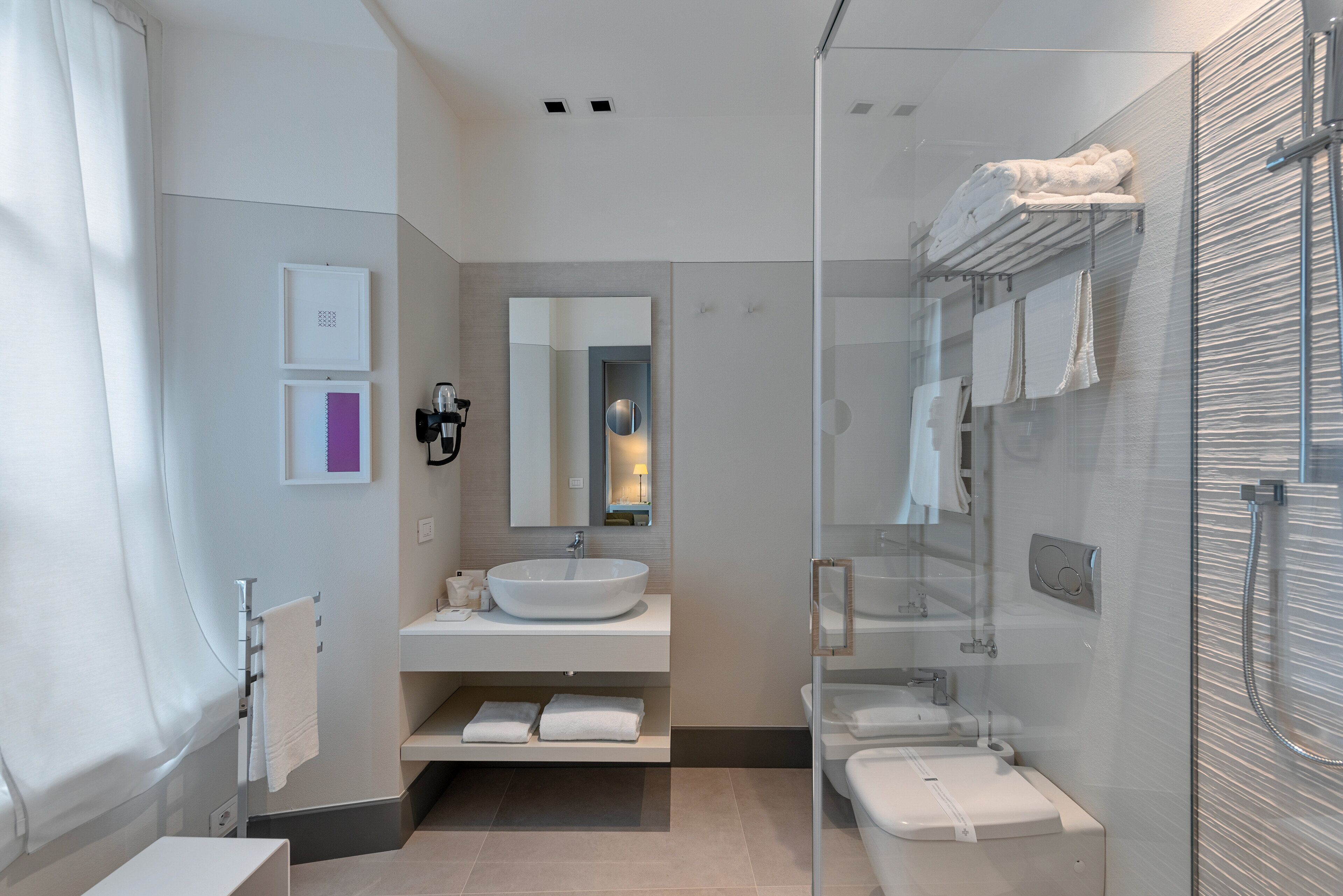 A modern bathroom with a large mirror, a vessel sink, a glass-enclosed shower, and neatly arranged towels.