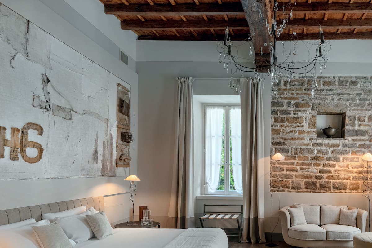 Un dormitorio con una cama grande, cabecera de madera, pared de piedra, candelabro y chimenea de piedra.