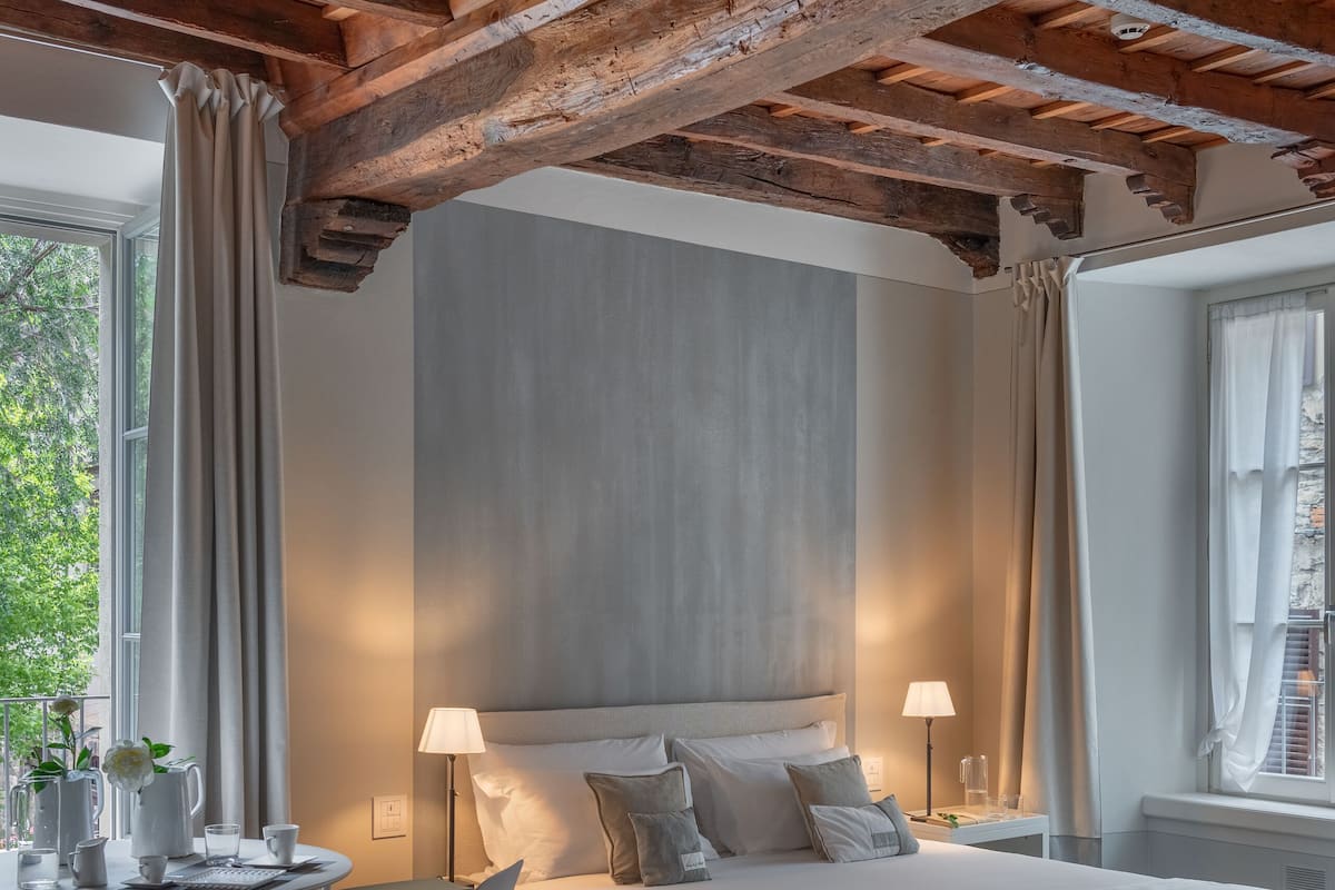 Un dormitorio con una cama grande, dos mesitas de noche, un escritorio con sillas y una ventana con cortinas.