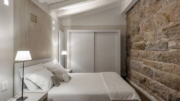 Un dormitorio con cama, lámparas de noche, armario y pared de piedra.