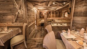 A rustic wooden interior with a long dining table set for a meal, wooden walls, and a high ceiling with exposed beams. - Sporthotel Romantic Plaza (Pinzolo)