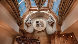 A cozy, circular seating area with a wooden floor, a small table with a bottle and glasses, and two cushions with deer designs. - Sporthotel Romantic Plaza (Pinzolo)