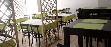 Un espace repas avec des tables et des chaises, un téléviseur fixé au mur et une cloison en bois.