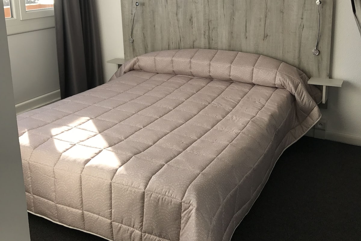 A bed with a wooden headboard, a window with curtains, and a small bedside table.
