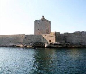 A historic stone fortress with a prominent tower, situated by a body of water. - Hôtel-Résidence les Aiguades (Port-de-Bouc)