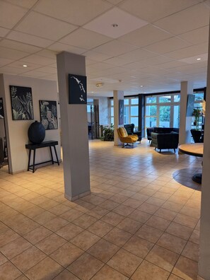 Un hall d’entrée spacieux avec un plafond haut, un sol carrelé et un mobilier moderne, notamment un fauteuil jaune et un canapé foncé.