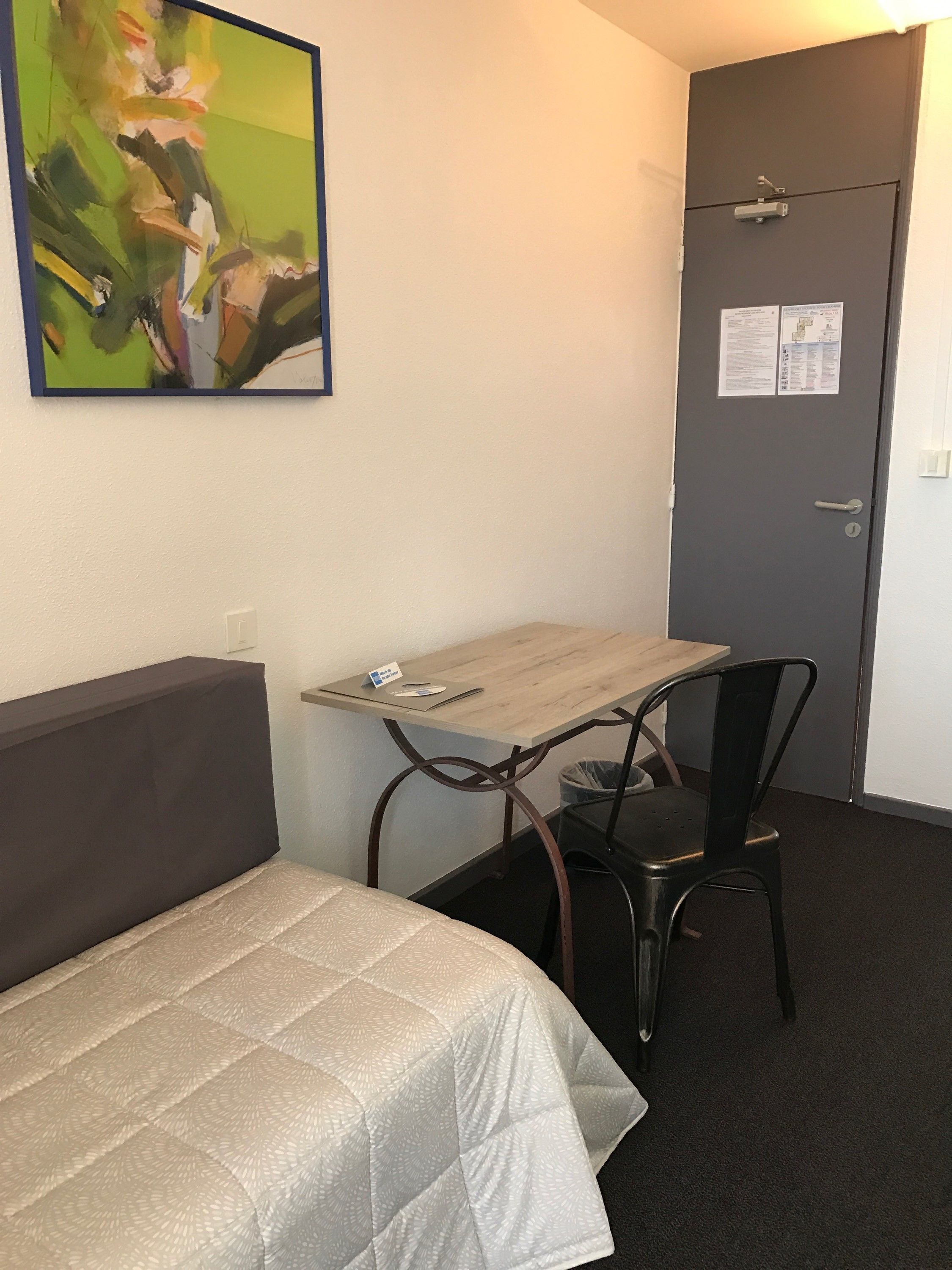 Une chambre d’hôtel avec un lit, un bureau, une chaise et une porte sur laquelle est affiché un avis.