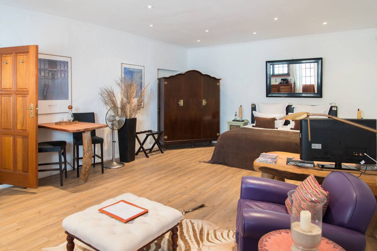 Una habitación con escritorio de madera, cama, sofá morado y televisor.