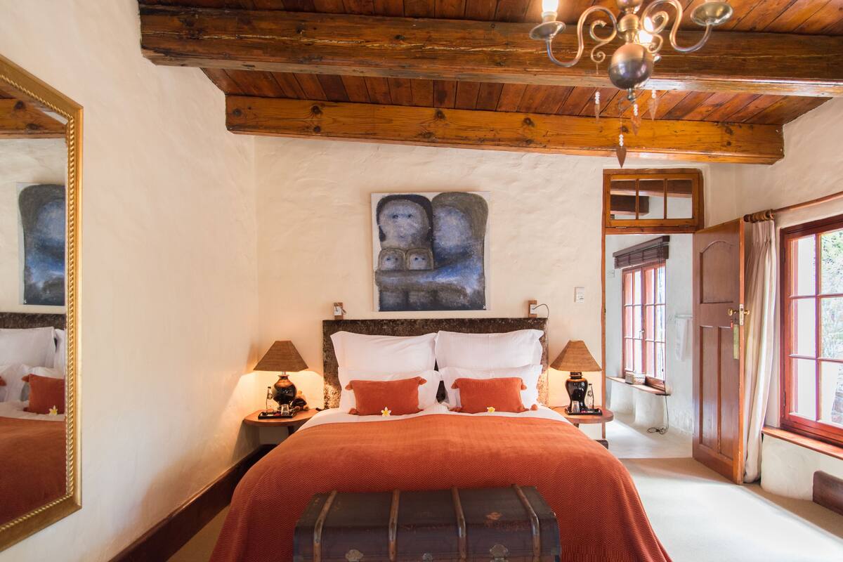 Un dormitorio con techo de madera, una cama grande con ropa de cama roja, una mesita de noche con una lámpara y un cuadro en la pared.