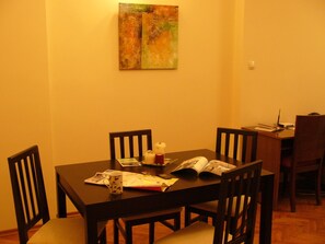 A dining area with a wooden table, four chairs, a painting on the wall, and a laptop on the table.