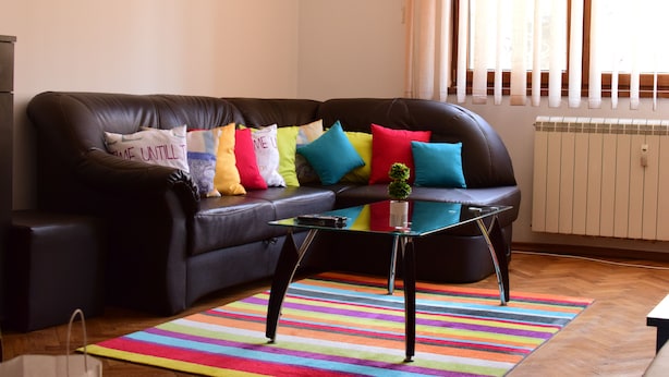 A living room with a black leather sofa, colorful cushions, a glass coffee table, and a striped rug. - BUZ Apart Sofia (Sofia)