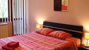 A hotel room with a bed, striped bedding, a nightstand with a lamp, and a window with blinds. - BUZ Apart Sofia (Sofia)