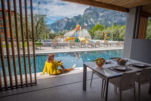 Zona junto a la piscina con vistas a montañas, una estructura de juegos acuáticos y un área de comedor con mesa y sillas.
