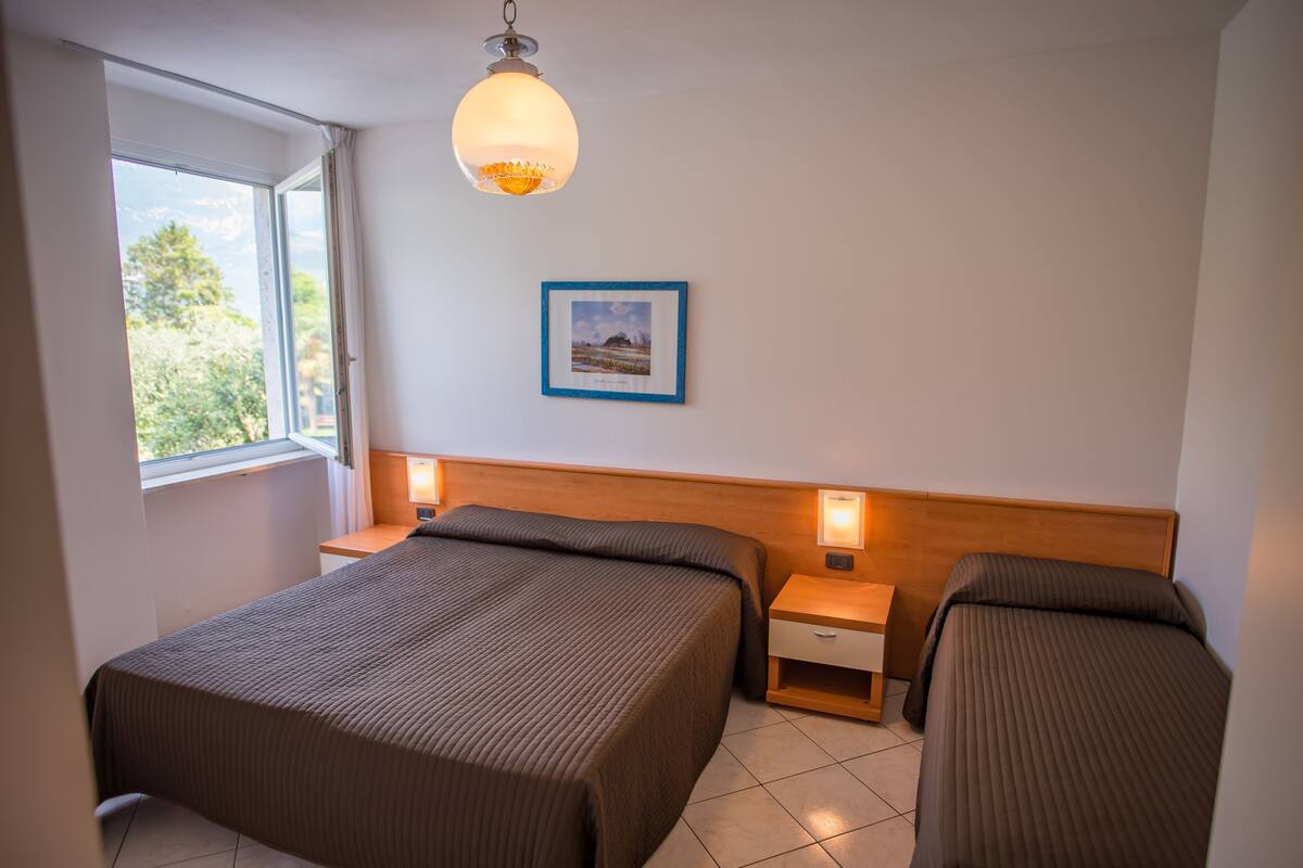 Ett sovrum med två sängar, ett fönster, en inramad tavla på väggen och en hängande lampa.