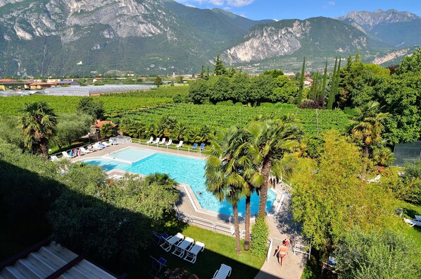 A pool surrounded by lush greenery and palm trees, with mountains in the background. - Residence Filanda (Riva del Garda)