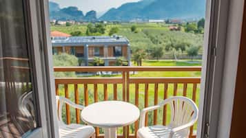 Ein Balkon mit Tisch und zwei Stühlen, der einen Blick auf eine grüne Landschaft und entfernte Gebäude bietet.