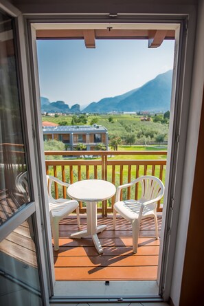 A balcony with a table and two chairs, offering a view of a green landscape and distant buildings. - Residence Filanda (Riva del Garda)