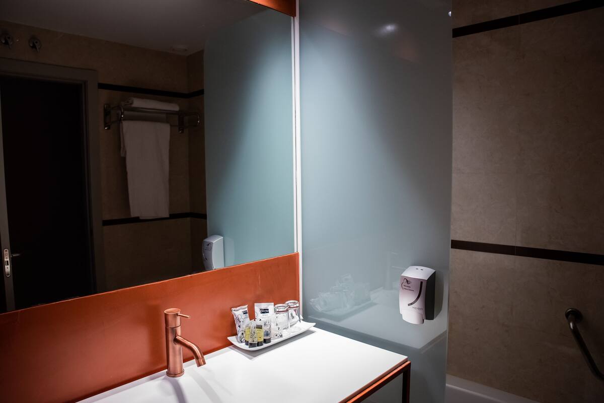 A bathroom with a white sink, a mirror, a towel rack, and a soap dispenser.