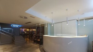 A modern reception area with a curved white counter, a staircase leading to an upper level, and a glass wall with a view of the interior. - Hotel Centro Los Braseros (Burgos)