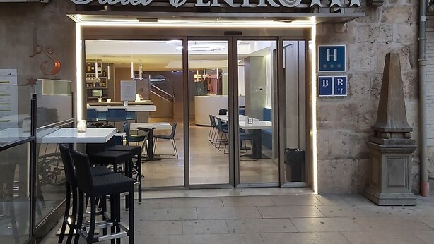 A hotel entrance with a glass door, a reception desk, and a seating area with tables and chairs. - Hotel Centro Los Braseros (Burgos)