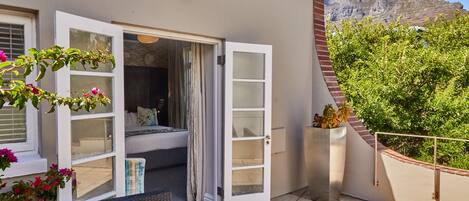 A balcony with a wicker chair, a white door, and a view of a mountain.