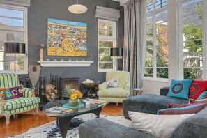 A living room with a fireplace, a large window, and a colorful painting on the wall.