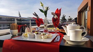 Un tavolo apparecchiato con diversi piatti, un servizio da tè e un vaso con fiori su un balcone con vista sulla città.