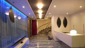 Un'accogliente hall d'albergo moderna con pavimento in marmo, una reception, una scala e pannelli decorativi a parete.