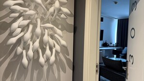 Un interno moderno con un'originale installazione artistica a parete, un corridoio ben illuminato e vista su un soggiorno con divano e tavolino.