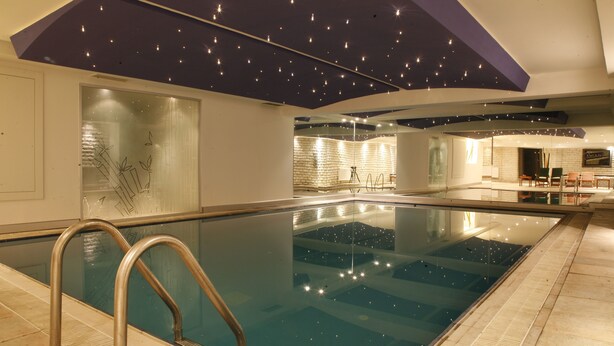 Una piscina interna con parete in vetro, ringhiere in metallo e un soffitto con luci simili a stelle.