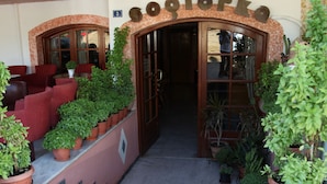 A building entrance with the sign "cociorka" above the door, surrounded by potted plants and red chairs. - Sogiorka Apartments (Hersonissos)