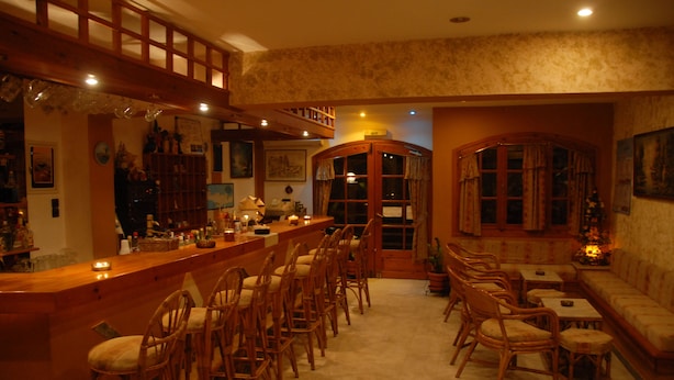 A cozy bar area with wooden furniture, a counter, and a seating area with cushioned benches. - Sogiorka Apartments (Hersonissos)