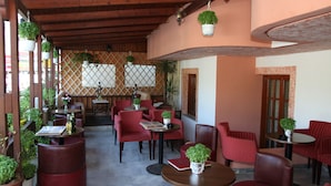 An outdoor cafe with red chairs and tables, potted plants, and a wooden ceiling. - Sogiorka Apartments (Hersonissos)