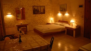 A hotel room with a bed, bedside tables, a mirror, a painting, and a dining table with chairs. - Sogiorka Apartments (Hersonissos)