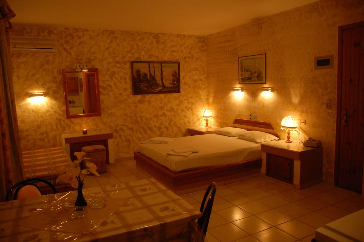 A hotel room with a bed, bedside tables, a mirror, a painting, and a dining table with chairs.