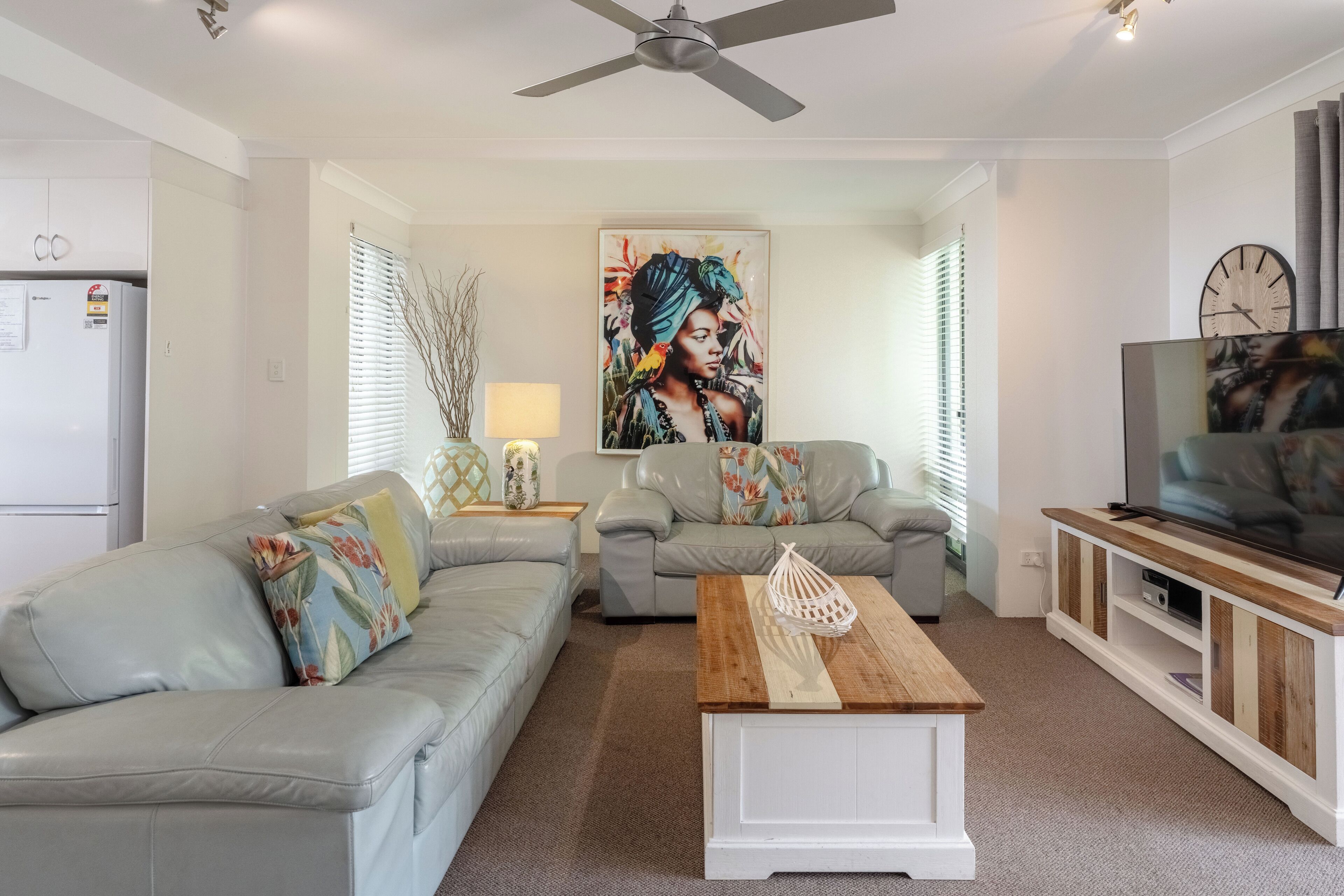 A modern living room with two grey sofas, a wooden coffee table, a TV on a wooden stand, and a large painting on the wall.