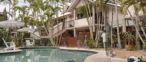 A pool area with lounge chairs, palm trees, and a building with balconies.