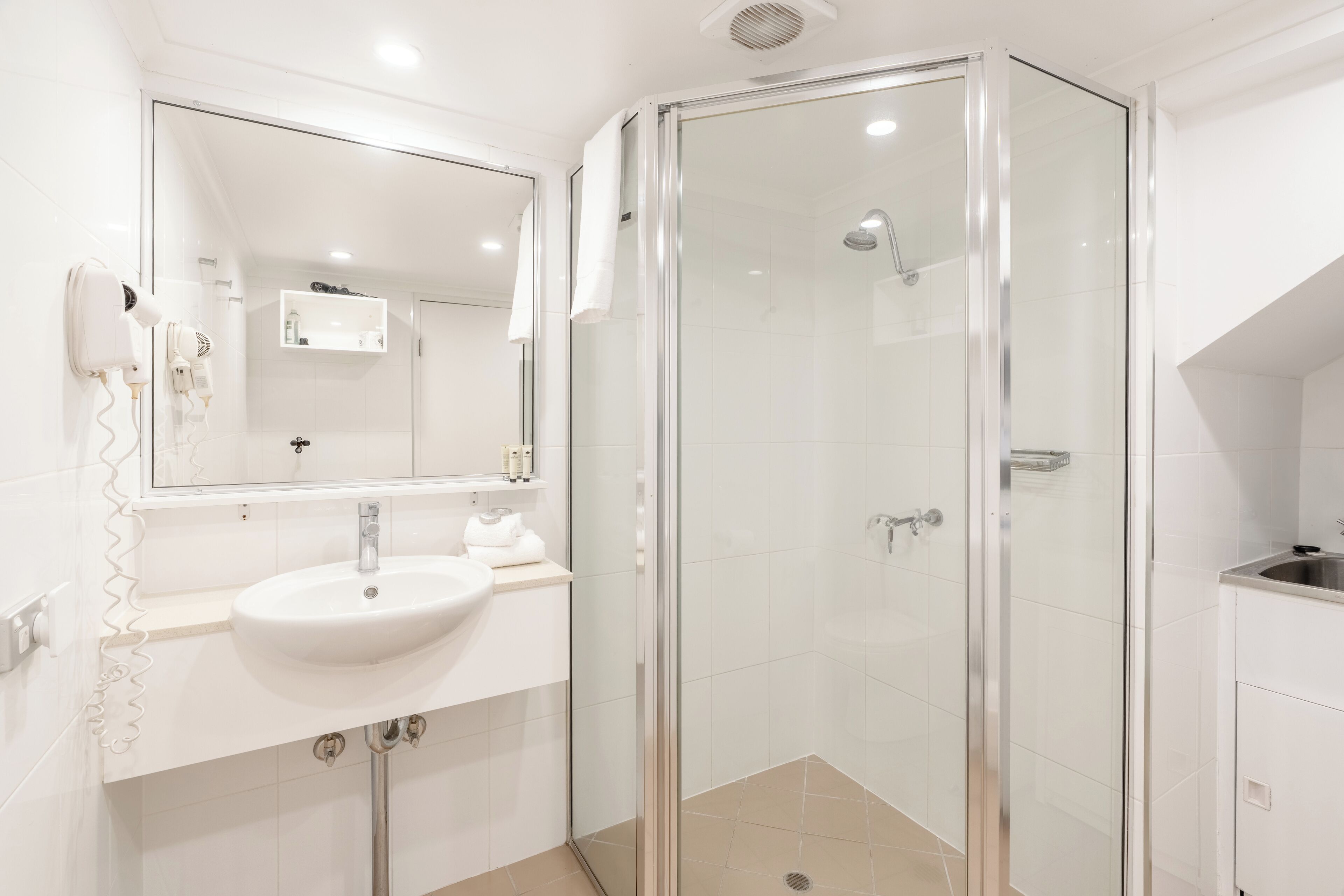 A modern bathroom with a glass-enclosed shower, a white sink, and a large mirror.