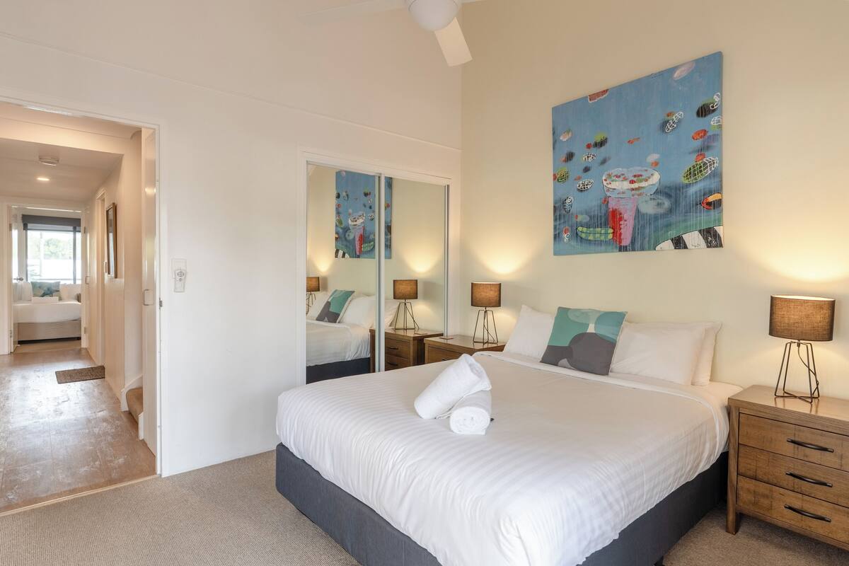 A hotel room with a large bed, a nightstand with a lamp, a mirror, and a painting on the wall.