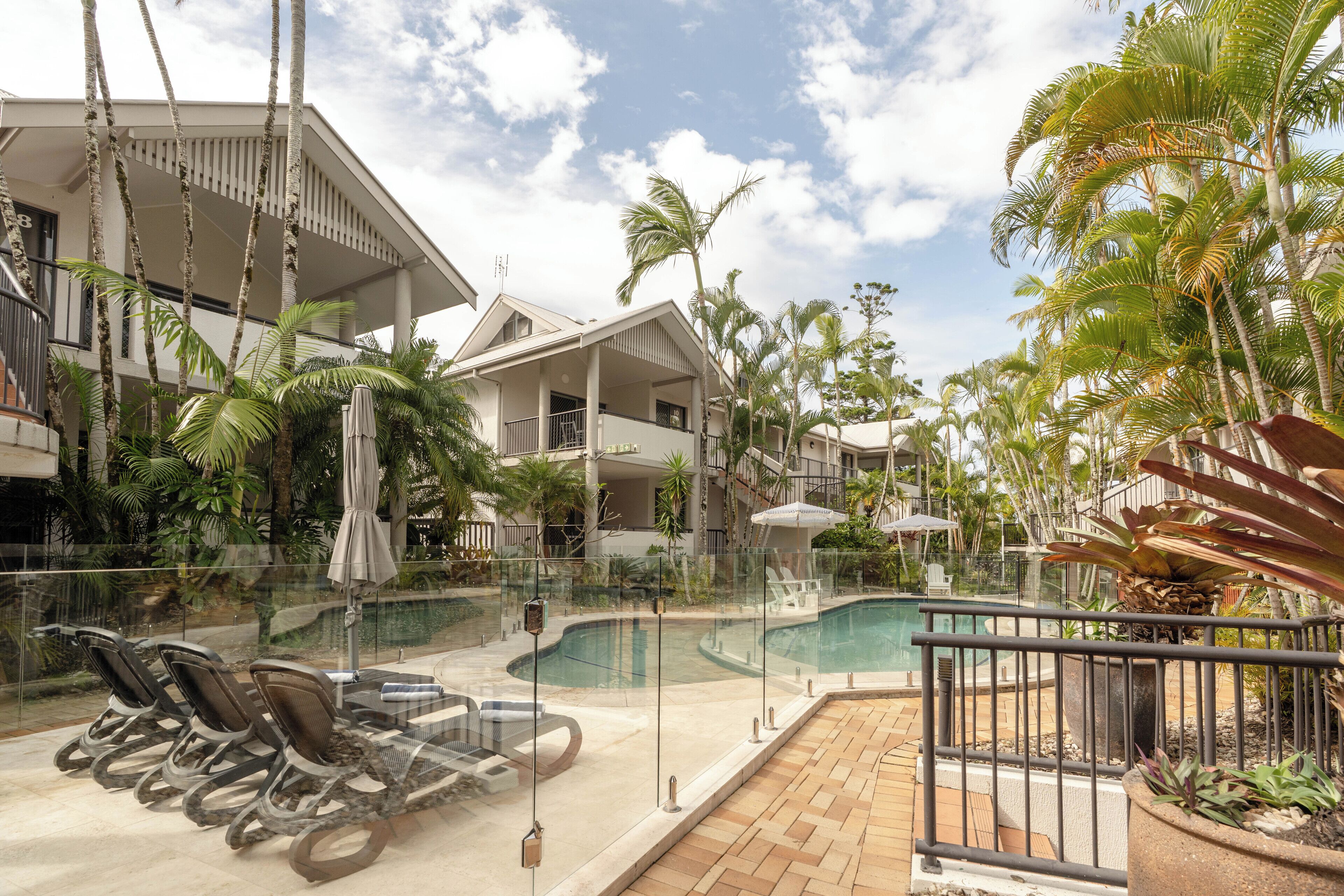 A pool area with lounge chairs, a glass railing, and palm trees.
