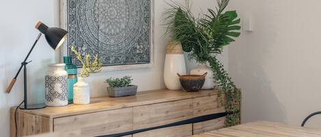 A wooden dining table with a bench, a decorative wall piece, a potted plant, and a lamp.