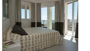 A hotel room with a bed, a nightstand, a lamp, and a window with a view of the sea. - Aparthotel Sheila (Jesolo)