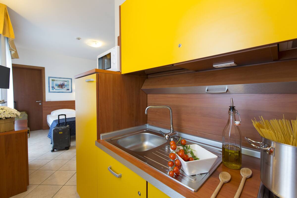 A compact kitchen with a sink, a bowl of cherry tomatoes, a bottle of olive oil, and a pot of spaghetti.