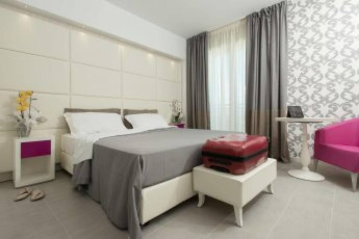 A modern hotel room with a bed, a nightstand, a small table, and a pink chair.