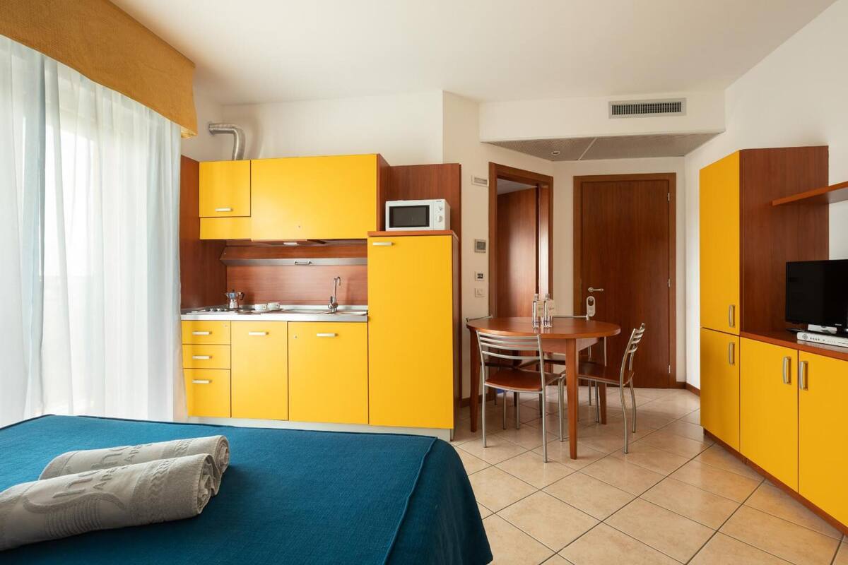 A compact hotel room with a bed, a kitchenette, a dining area, and a TV.